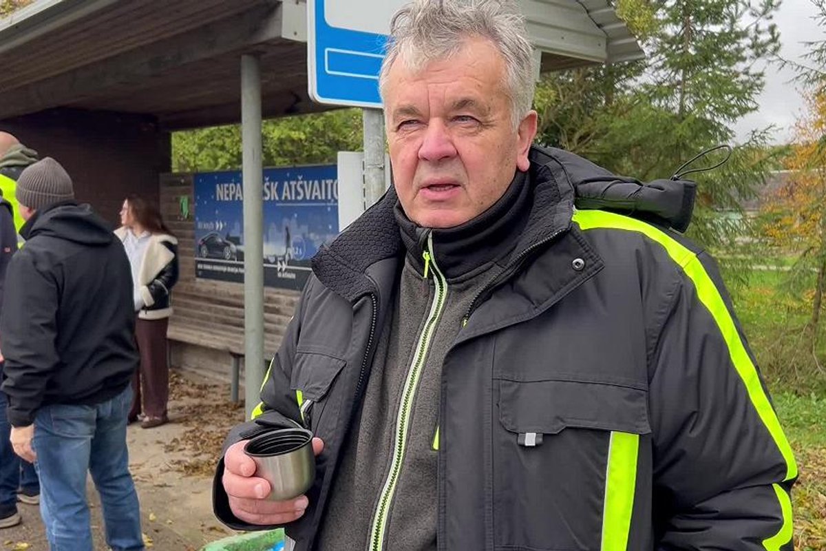 A man drinking from a thermos at a bus stop