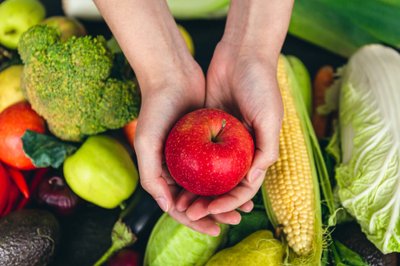 Close-up, an apple in a female hand on a blurred background with vegetables, the concept of nutrition and health.