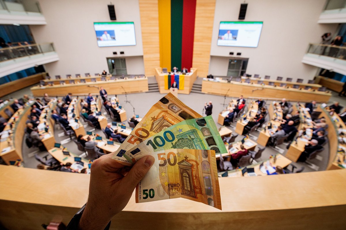 A hand holding euro banknotes in front of a parliament